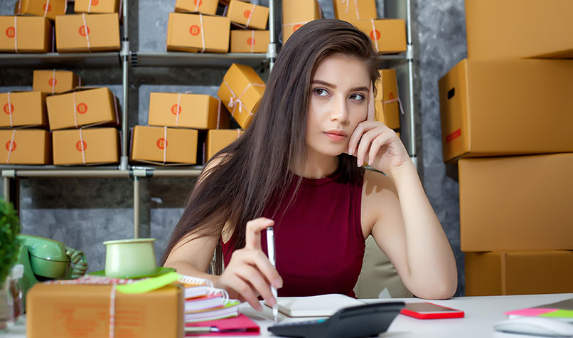 A worried businesswoman deep in thought in front of shelves of boxes