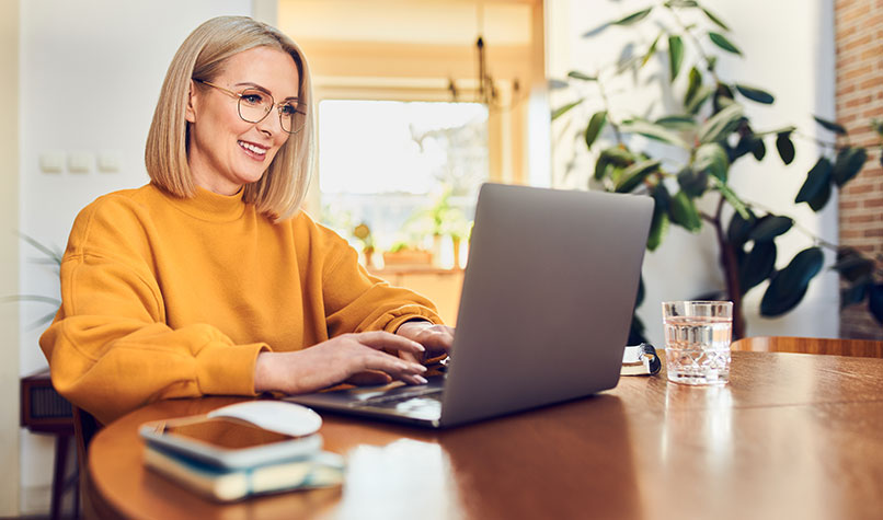 Woman working at a table while smiling at her laptop