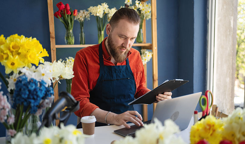 A male florist checking his tablet computer against a laptop