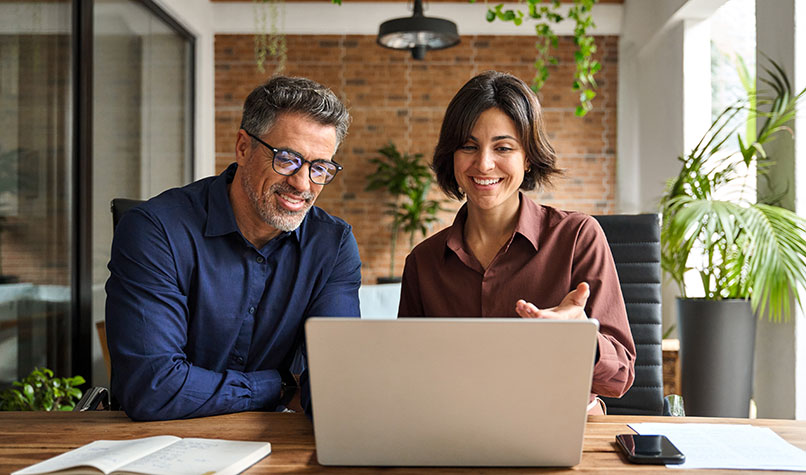 A man an a woman smiling while looking at a laptop