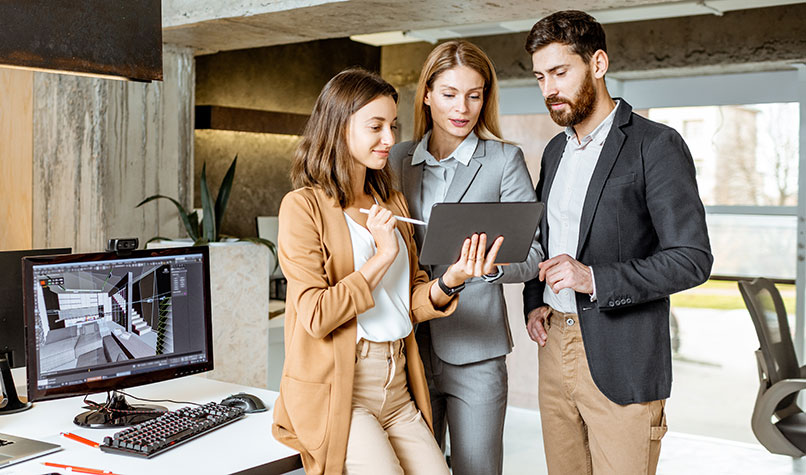 Two women and a man discussing something on a tablet computer