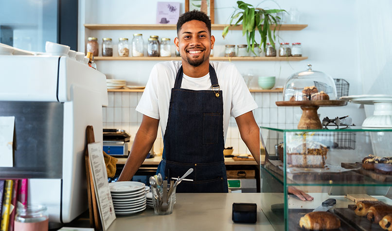 A smiling coffee shop owner standing behind the counter.