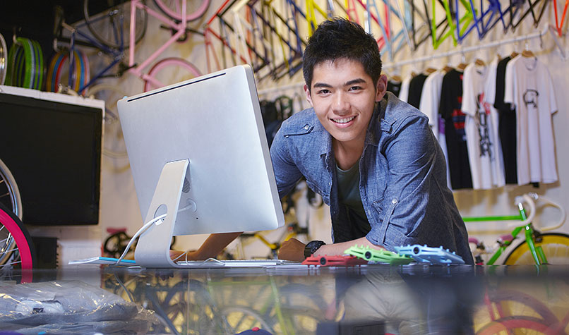 Bicycle shop owner leaning on his sales counter with multi-coloured bikes behind him