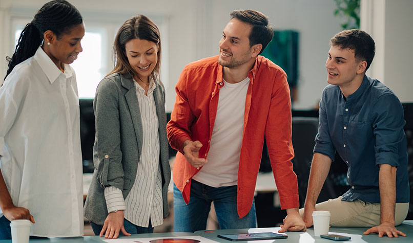 Five people discussing charts on a table they are standing behind.