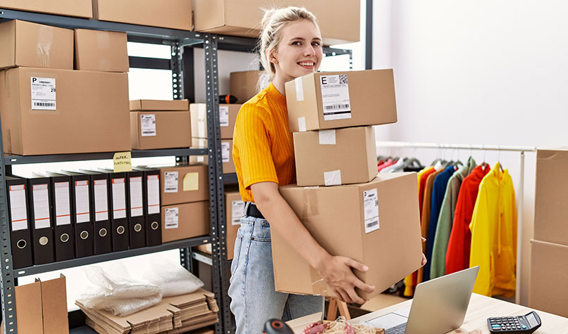 Woman wearing a yellow top carrying a pile of brown boxes