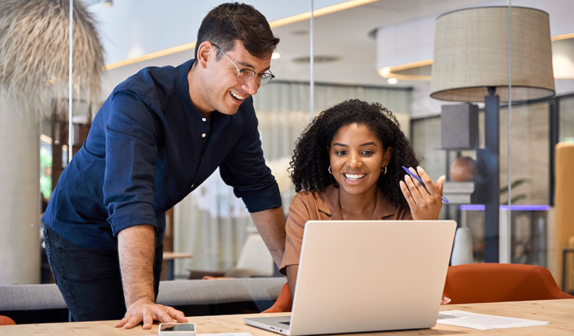 A man leaning over a desk and looking at a laptop with his female colleague