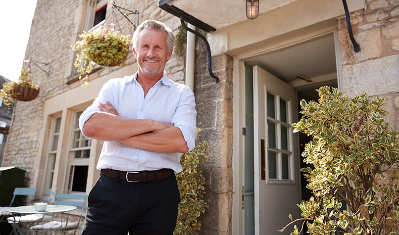A landlord with white hair standing outside a property
