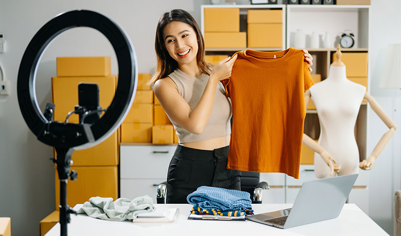 Woman holding up an orange jumper to a ring light