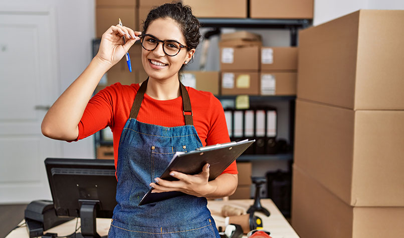 Woman with glasses wearing an apron and red jumper holding a clipboard