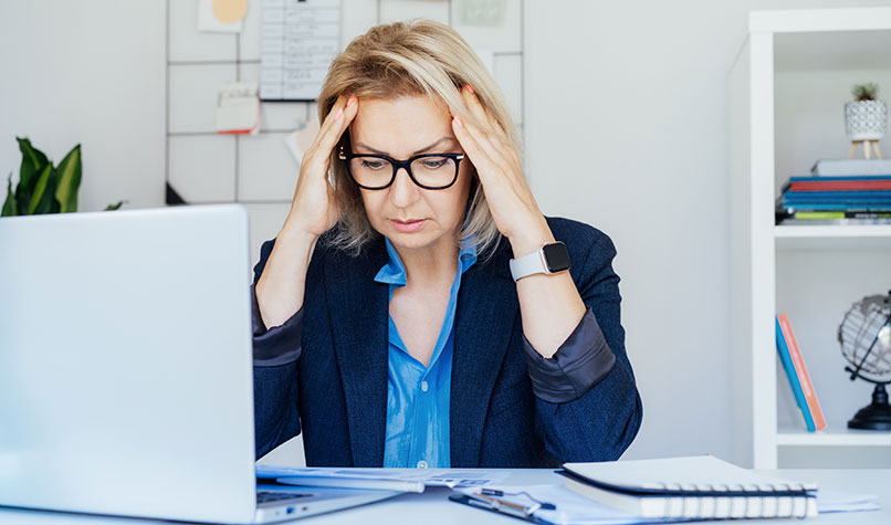 Woman holding her head at a desk with a laptop computer