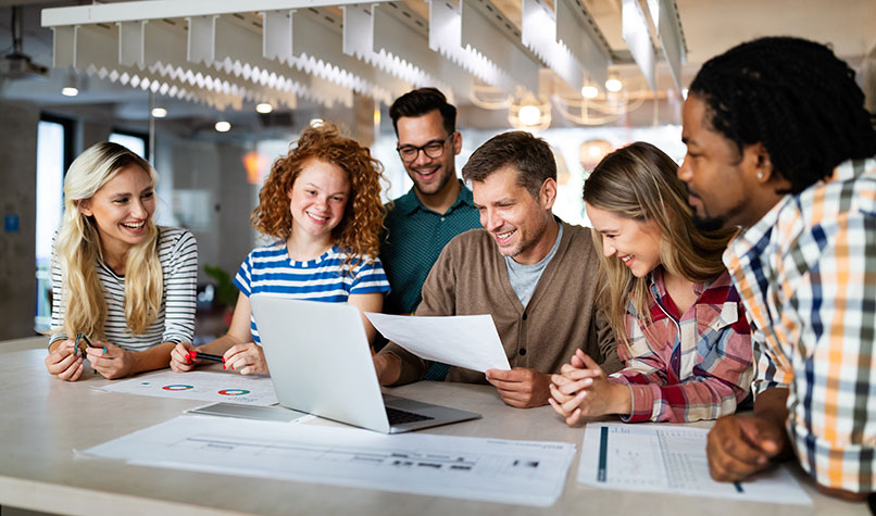 A diverse group of employees sat around a table with their employer who is holding a document.