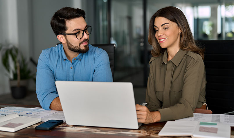 Two people sitting at a laptop discussing something on the screen.