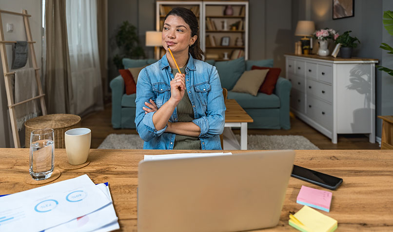 Woman wearing a blue shirt sat at a desk with a laptop in the foreground.