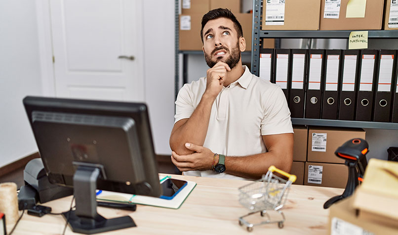 Worried man sat at a desk pondering what he has seen on his laptop.