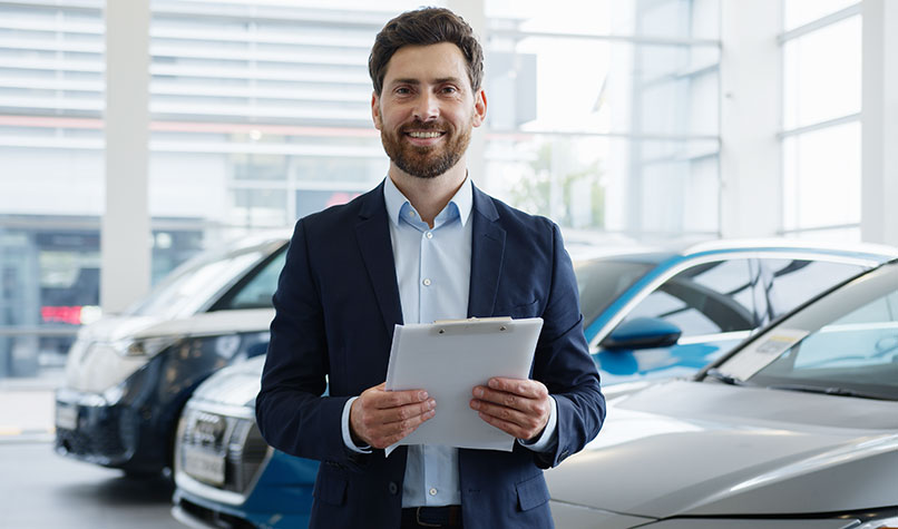 Man holding a clipboard standing in a car showroom.