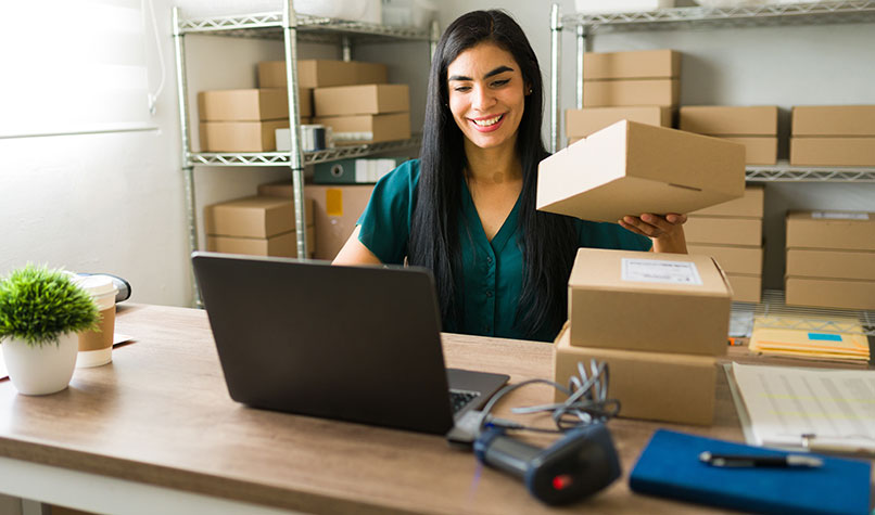 A woman with a pile of boxes looking at a laptop.