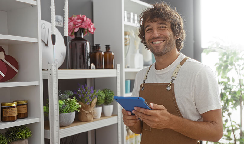 Smiling man wearing an apron stood in front of shop shelves with assorted ornaments.
