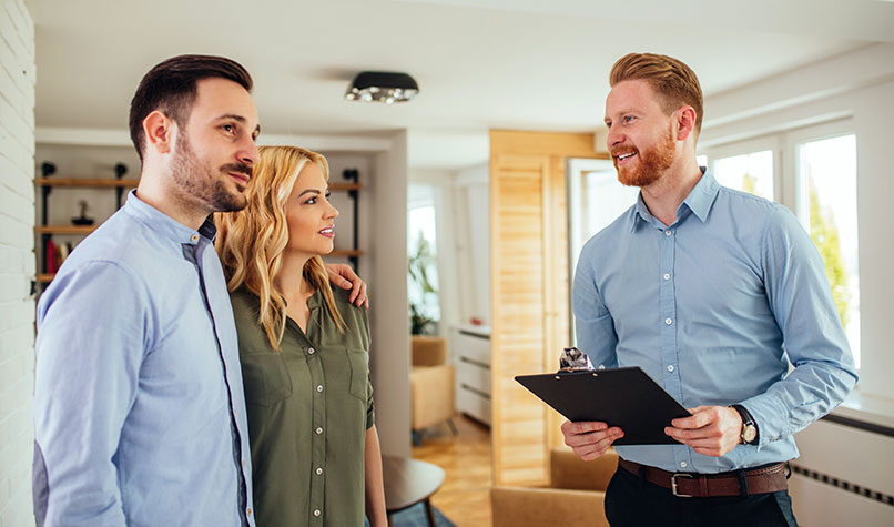 A male and female couple talking to a male landlord holding a clipboard.