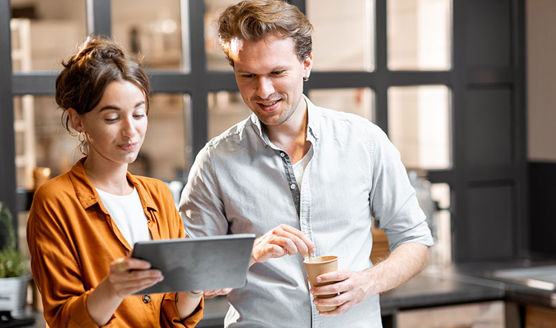 A man and a woman standing up looking at a tablet computer
