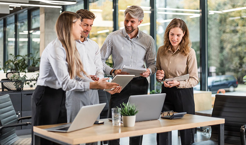 Four employees gathered around a desk smiling while looking at a document.