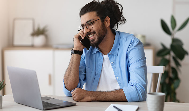 Man wearing glasses sat at his desk taking a call on his mobile phone