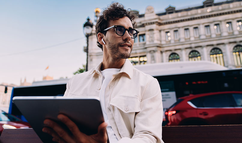 A man sat outside looking away from a tablet computer on his lap.
