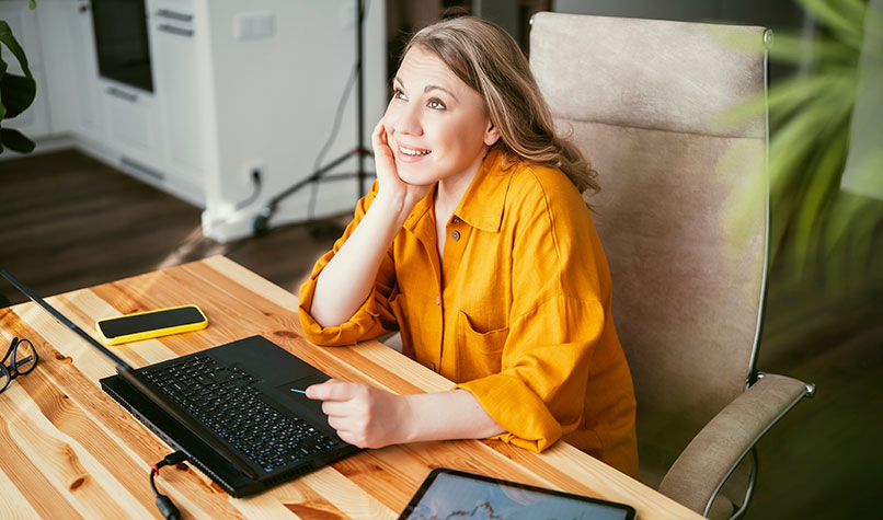 Woman wearing a yellow blouse sat at a desk with her laptop