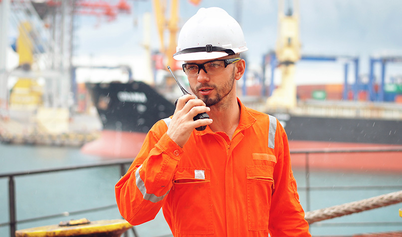An oi rigger in an orange jumpsuit using a walkie talkie
