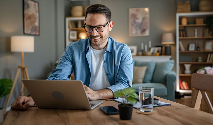 A man in his dining room looking at the screen on his laptop