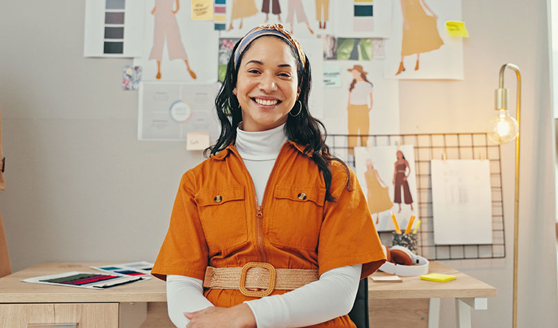 A woman in an orange jumpsuit in front of some fashion drawings.