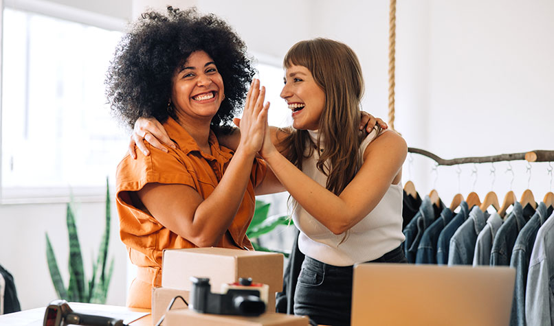Two happy women high fiving each other in a clothes shop.