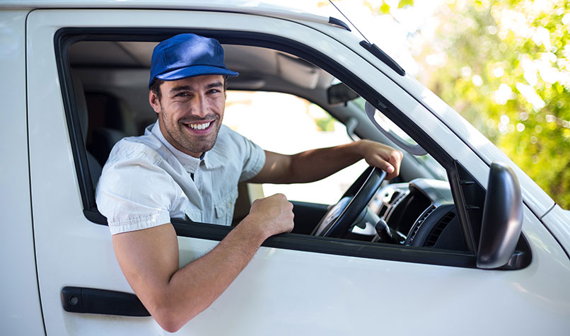 A workman hanging out of the window of his white van.