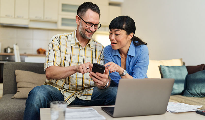 A man and woman sat on a sofa looking at a mobile phone.