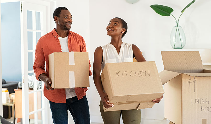 A couple carrying boxes into an empty room in a house.