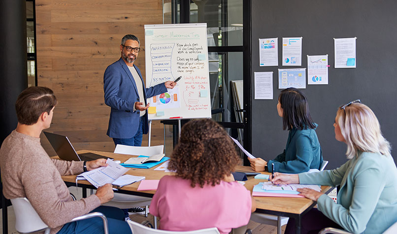 A man using a white board to give a presentation to officer workers