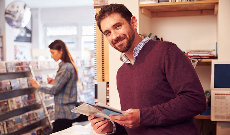 Owner of a record shop stood behind the counter holding a seven inch vinyl record.