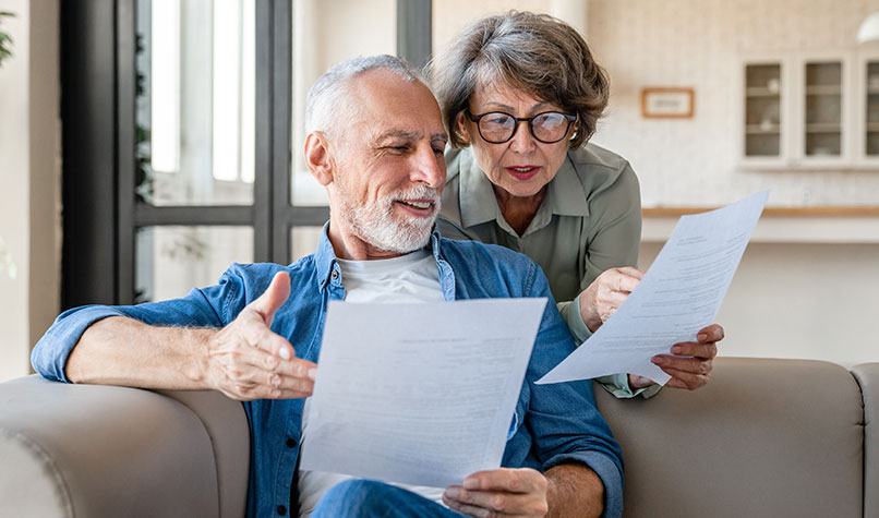 An elderly couple looking at official looking letters while sat on a sofa